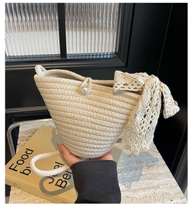 Detail of cream woven bucket bag featuring pearl closure and large lace bow detail