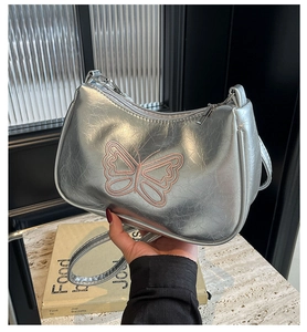 Detailaufnahme der silbernen Y2K-Handtasche mit rosa Schmetterlingsstickerei und Metalloptik