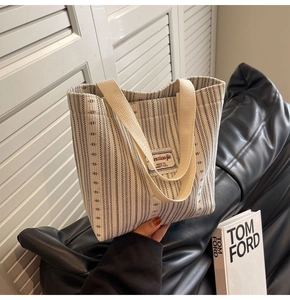 Detail of striped canvas tote bag with beige handles and woven brand logo tag