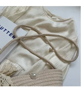 Detail of woven crossbody bag featuring lace trim, pearl clasp and soft rope strap