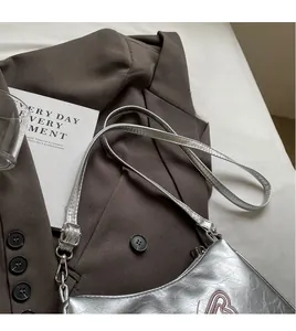 Detail der silbernen Umhängetasche mit Knitteroptik, R-Logo auf einem dunklen Blazer