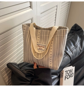 Detail view of off-white vertical striped canvas tote bag with woven brand label