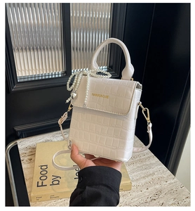 Detailed view of a white crocodile pattern box bag with a gold handle and pearl charm