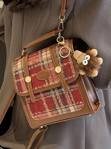 Retro-Umhängetasche aus braunem Leder und Tweed mit Plüsch-Anhänger auf Mantel