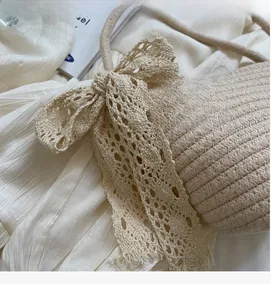 Detail of beige hand-woven straw bag with lace bow decoration and pearl accent