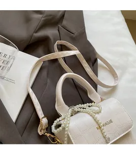 Detail of white crocodile texture handbag featuring pearl chain and brand logo