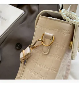 Detail of beige crocodile embossed bag featuring elegant pearl handle and gold hardware