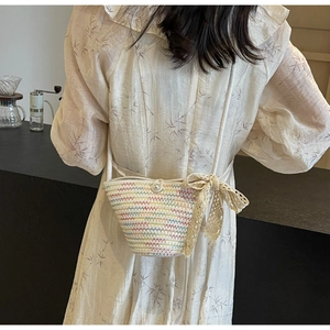 Detail of woven crossbody bag featuring lace bow and pearl buckle on a female model