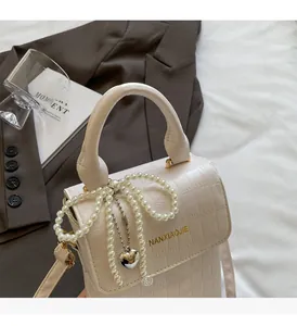 Detail of beige crocodile pattern bag with pearl bow and heart metal pendant