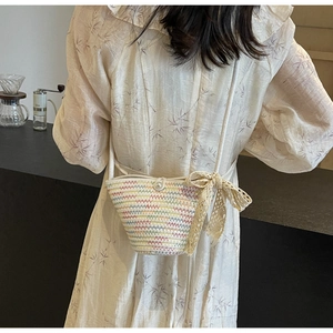 Detail of hand-woven straw crossbody bag with colorful stripes, pearl button and lace bow
