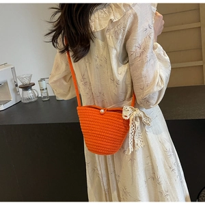 Detail of orange hand-woven crossbody bucket bag with pearl button and lace bow accent