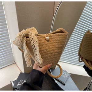 Close-up of woven bucket bag featuring delicate beige lace bow and pearl button detail