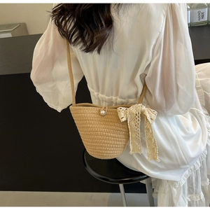 Detail of handmade straw crossbody bag featuring pearl closure and lace bow decoration