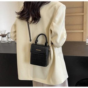 Detail of black crocodile texture crossbody bag with gold logo on beige blazer
