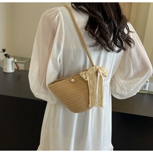 Detail of straw woven crossbody bag with lace bow, pearl button and textured fiber