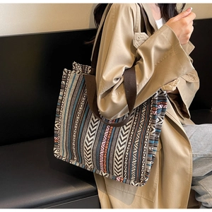 Ethnic woven tote bag with colorful geometric patterns shown on shoulder with beige coat