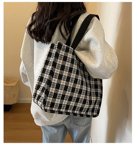 Close-up of black and white checkered tote bag with wide shoulder strap on a model