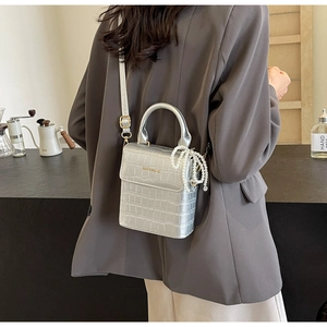 Detail of silver crocodile-embossed mini bag featuring a pearl chain and round handle