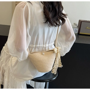 Detail of hand-woven straw crossbody bag with pearl button and lace bow on beige dress