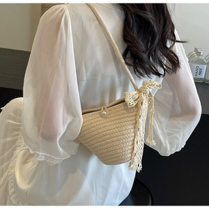 Detail of hand-woven beige crossbody bag with pearl button closure and lace bow accessory