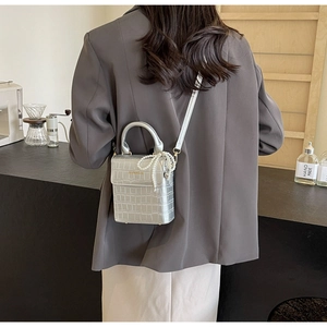 Silver crocodile texture mini bag with pearl bow charm worn on shoulder in a cafe setting