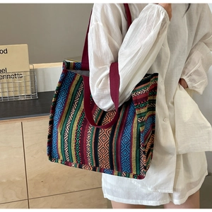 Ethnic woven tote bag with colorful geometric patterns and burgundy strap shown on shoulder