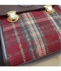 Close-up of red tartan fabric backpack with brown leather trim and gold metal buckles