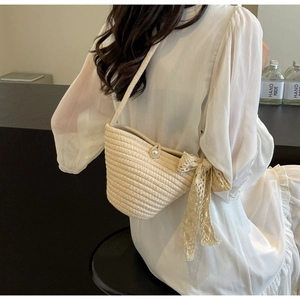 Detail of hand-woven off-white crossbody bag with pearl clasp and lace bow accessory