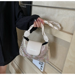 Detail der floralen Baguette-Tasche mit weißem Flechtriemen und silberner Kette