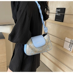 Détail du sac sous le bras bleu clair avec texture florale dorée et chaîne à breloque cœur