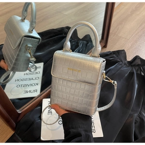 Detail of silver crocodile-embossed mini bag with metallic finish and gold logo text