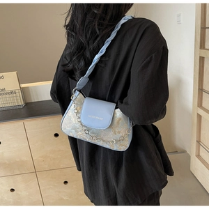 Détails de broderie florale bleue et bandoulière tressée sur ce sac sous l'aisselle