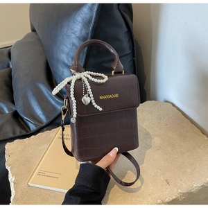 Detail of dark brown crocodile pattern bag with pearl bow charm and heart pendant