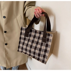 Detail of vintage plaid tote bag with brown straps held by a model in a trench coat