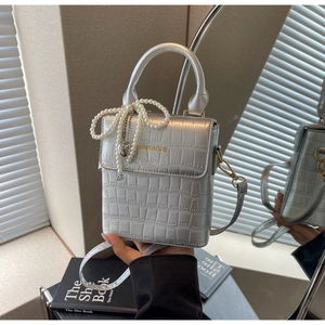 Detail of silver crocodile-embossed crossbody bag with pearl bow and heart charm decoration
