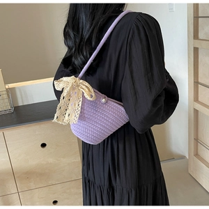 Detail of purple woven shoulder bag featuring a large beige lace bow and pearl button