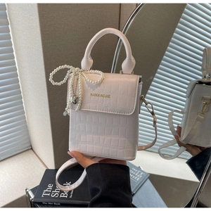 Detail of white crocodile pattern leather bag with pearl bow and heart charm on mirror
