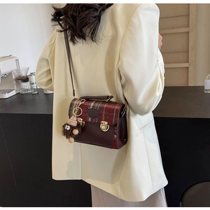 Close-up of retro crossbody bag with brown plaid pattern and plush charm on a model