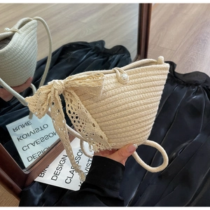 Detail of straw woven bag featuring delicate lace bow, tassel fringe and pearl buckle
