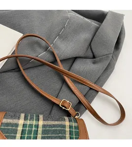 Detail of adjustable brown leather shoulder strap with gold buckle on plaid crossbody bag