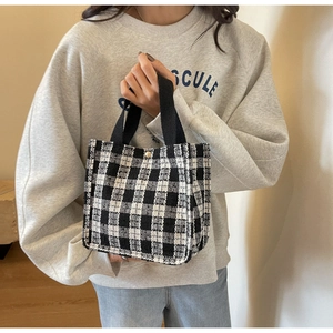 Detail of checkered tote bag featuring a round gold metal buckle and woven handles
