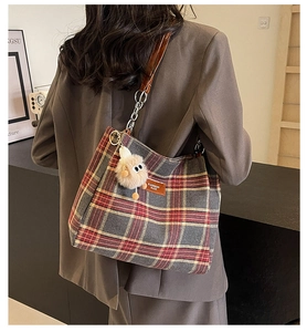 Detail of red plaid tote bag with brown leather strap and cute plush charm