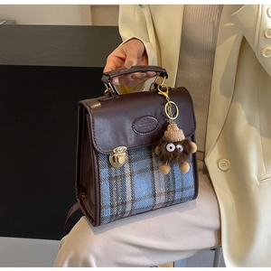 Detail of retro plaid messenger bag with brown leather trim and cute plush monster charm
