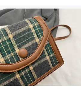 Macro view of British style green plaid fabric and brown leather stitching on crossbody bag