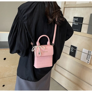 Pink croc-embossed crossbody bag featuring a pearl bow charm and top handle detail