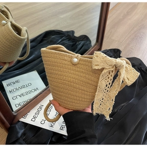 Macro detail of hand-woven straw handbag featuring lace bow and pearl button closure