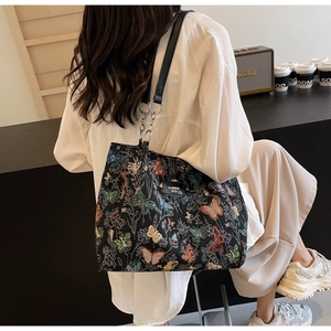 Close-up of black tote bag featuring colorful butterfly embroidery and silver chain strap