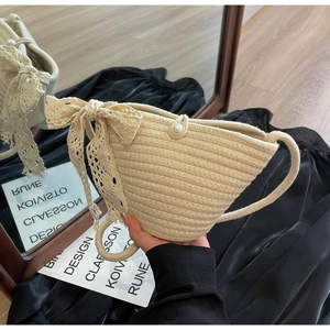Detail of hand-woven beige crescent bag with white lace bow and elegant pearl buckle