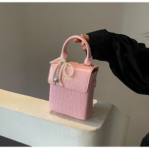 Detail of pink croc-embossed mini bag with pearl bow and silver heart pendant charm