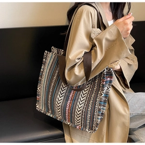 Ethnic woven tote bag with colorful stripes and brown strap shown on model shoulder